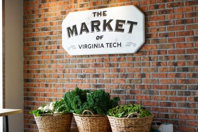 Three baskets of vegetables sit against a brick wall, below a sign that reads "The Market of Virginia Tech."